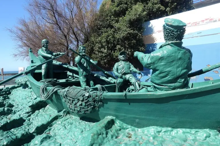 Escultura em bronze esverdeado de pescadores num barco a remos, na Praia da Aguda