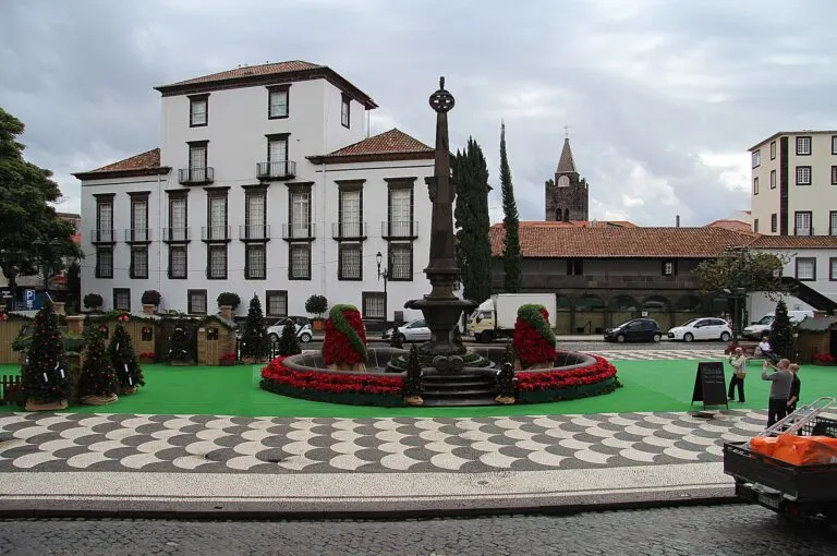 Casinhas de madeira, árvores de Natal e o chafariz rodeado de poinsétias na Praça do Município, no Funchal, com a torre da Sé ao fundo
