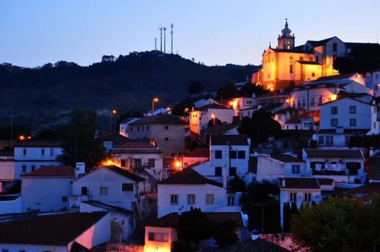 Alenquer ao anoitecer, com o casario iluminado e a Igreja de São Pedro no alto da encosta