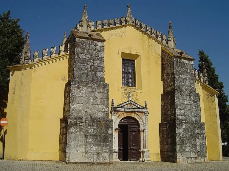 Fachada amarela de uma igreja em Alvito, com contrafortes de granito, ameias e portal de pedra