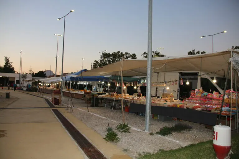 Bancas de doces e frutos secos da Feira Nova de Outubro iluminadas ao anoitecer, no Parque Urbano de Alcácer do Sal