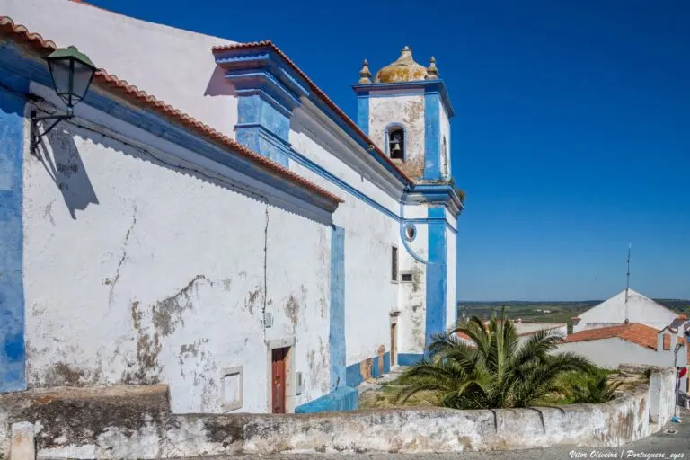 Fachada lateral da igreja matriz de Aljustrel, caiada de branco com barras azuis e a torre sineira