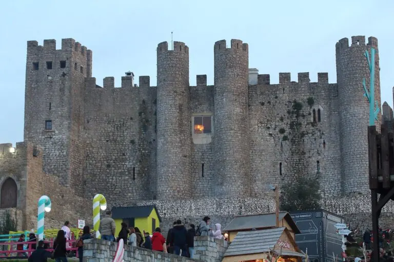 Castelo de Óbidos ao entardecer, com as casinhas de madeira e os enfeites do mercado de Natal junto às muralhas
