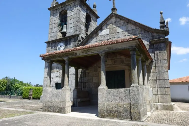 Fachada de granito da igreja paroquial de Espinho, em Braga, com o alpendre de colunas e o relógio da torre