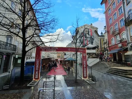 Pórtico de entrada do Mercado de Natal de Coimbra na Praça do Comércio, com as casinhas de madeira ao fundo, em dezembro de 2022