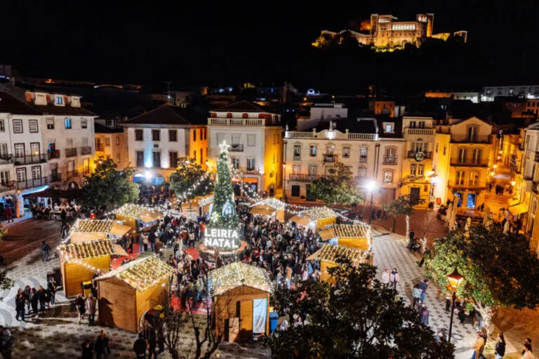 Casinhas de madeira iluminadas e árvore de Natal numa praça do centro histórico de Leiria, com o castelo ao fundo