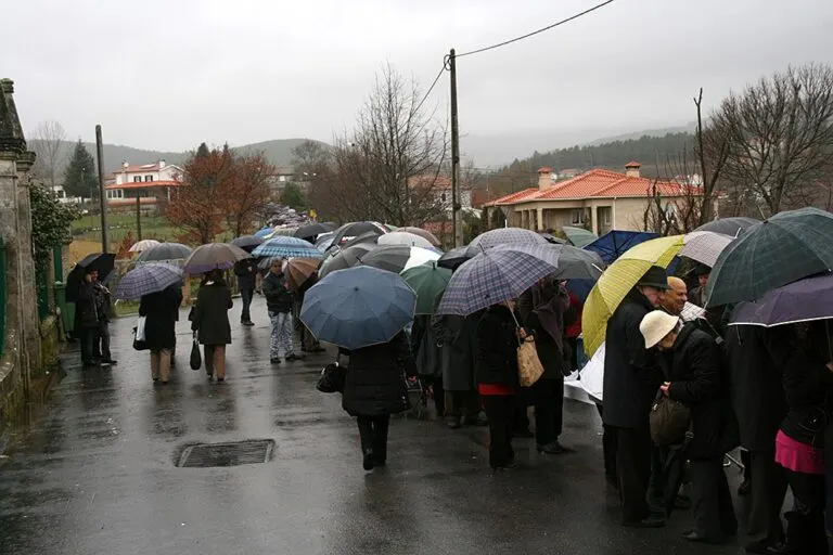 Visitantes de guarda-chuva ao longo da mesa comunitária na rua de Vila Grande, no dia de São Sebastião