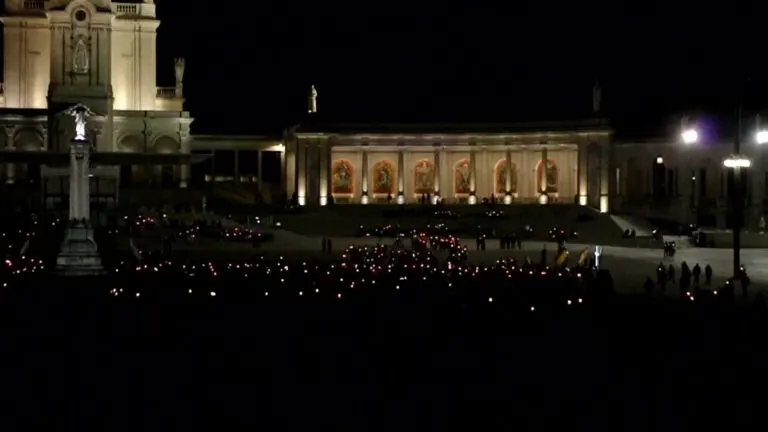 Procissão das velas à noite no Recinto de Oração do Santuário de Fátima, com a colunata iluminada ao fundo