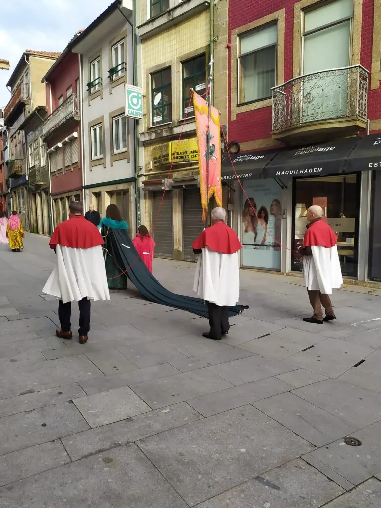 Irmãos de capa vermelha e branca e estandarte na procissão de São Vicente de 2024, numa rua de Braga
