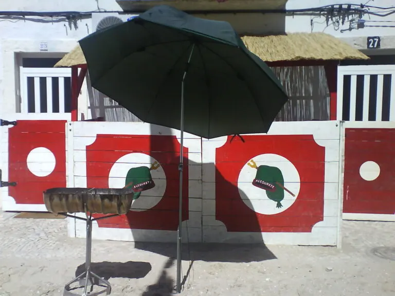 Tronqueiras de madeira pintadas de vermelho e branco com o barrete verde e o nome de Alcochete, à porta de uma casa